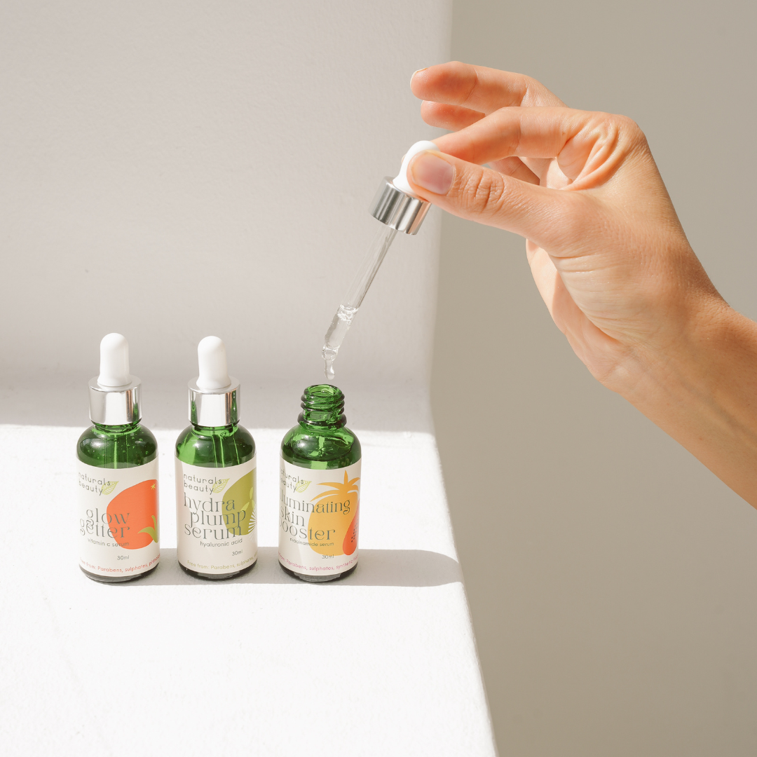 Hand using a dropper to apply serum from a bottle with other bottles in the background.