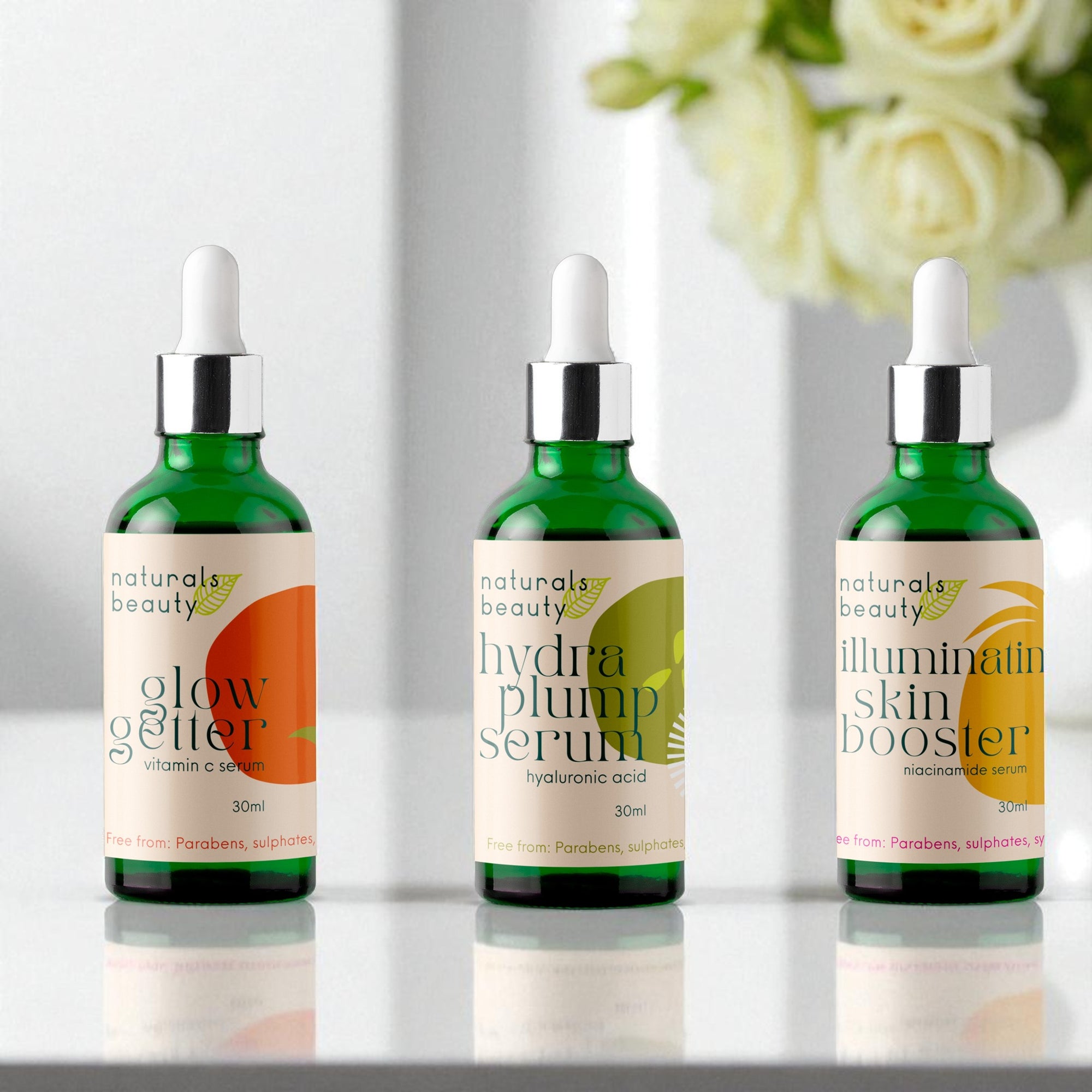 Three green serum bottles with labels on a reflective surface, with flowers in the background.