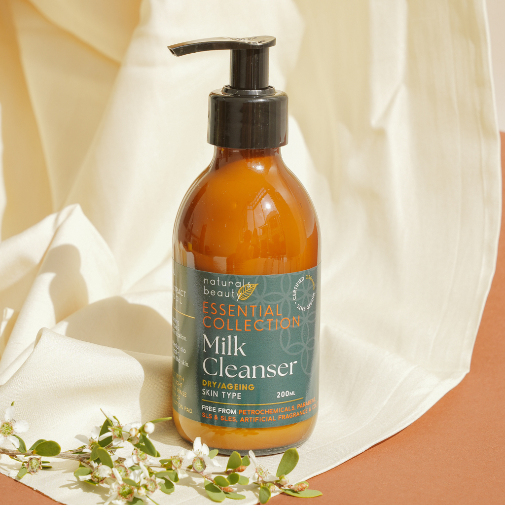 Bottle of Milk Cleanser from Naturals Beauty Essential Collection on a soft fabric background